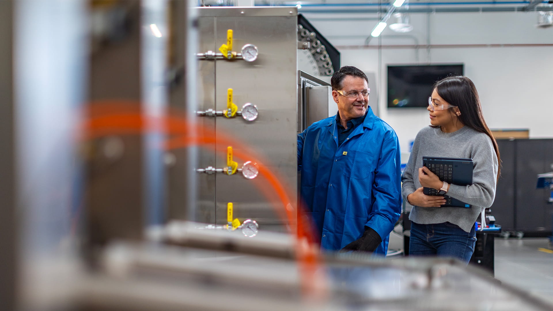 Adult male and adult female wearing safety glasses looking at each other in a factory.